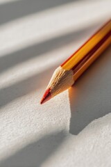Close-up of a red and yellow pencil on textured paper surface with shadows
