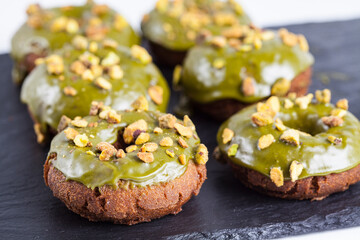 Six pistachio donuts with nuts on a black slate. 