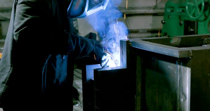 Industrial electrogas welding. A worker welds metal in a protective helmet. Heavy industry and metallurgy. Professional at work. Close-up 4k footage.