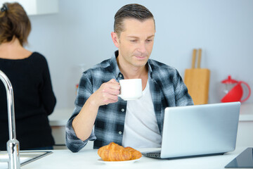 Man eating breakfast looking at laptop