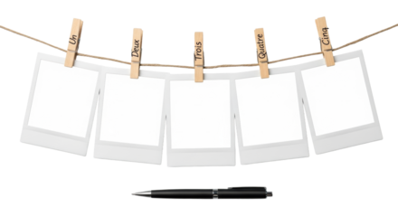 Five blank instant photo frames, Polaroid-style, with handwritten 'Un' to 'Cinq' on wooden clothespins, suspended by twine, a black pen below, on a seamless transparent background, commercial product