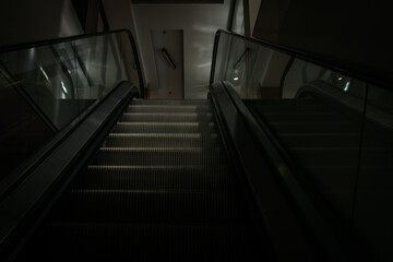 Escalator leading downwards in a modern building, illuminated by soft lighting, showcasing sleek design and glass railings, creating a contemporary atmosphere with copy space