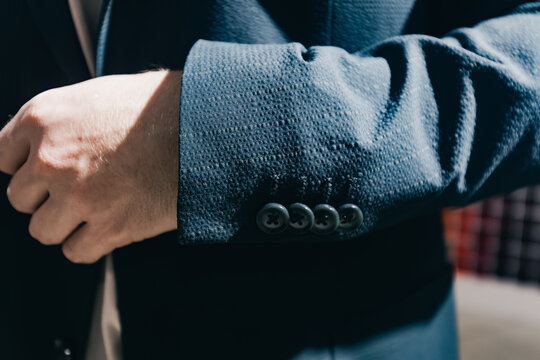 Close-up of a well-dressed man adjusting the cuff of a tailored blue suit jacket, showcasing fine fabric texture and elegant design elements in a stylish environment