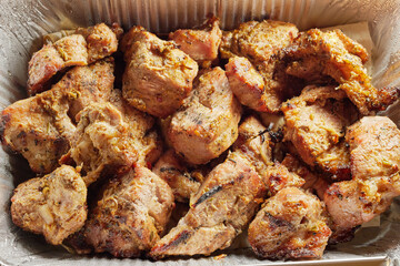 Close-up of grilled shashlik kebab pieces in a foil tray