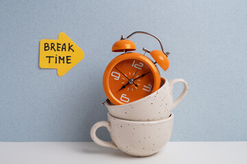 Orange alarm clock with "Break Time" note on stacked coffee cups. Time for a break. 