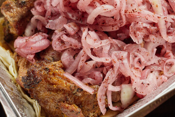 Close-up of grilled shashlik kebab pieces with marinated onions in a foil tray