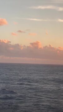 Calm ocean waters reflect the warm hues of sunset. The horizon is filled with soft clouds, creating a peaceful atmosphere during the evening
