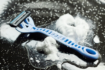 Close-up of a disposable razor on a wet black surface with shaving foam.