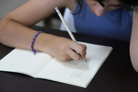
Teenager drawing a human figure in a notebook with a pencil
