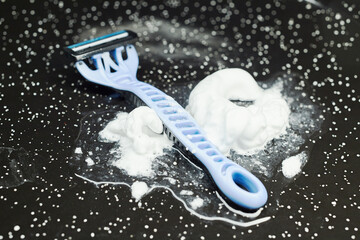Close-up of a disposable razor on a wet black surface with shaving foam.