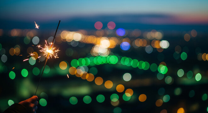 Sparkler in hand with blurred city lights background, creating a festive atmosphere, representing celebration, party, and holiday, perfect for event promotion