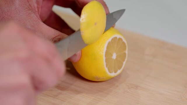 Detailed close-up shot of person skillfully slices a ripe lemon sliced with knife on wooden cutting board. Ideal for themes related to fresh ingredients, healthy cooking, citrus recipes, detox drinks.