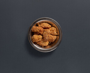 A bowl filled with crunchy golden nuggets is placed on a dark surface. This snack is perfect for sharing during gatherings or enjoying alone.