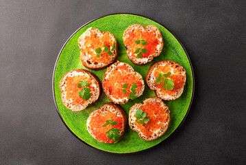 Fresh homemade canape made from full grain baguette, butter and salmon caviar deocrated with aromatic thyme twigs on bright ceramic plate top view.