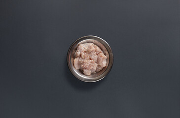Raw chicken pieces are neatly arranged in a metal bowl, sitting on a dark surface in a kitchen environment. The chicken is ready for cooking in various recipes.
