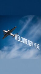 Airplane with banner and writing the phrase "Welcome New Year" in smoke in the sky. Abstract image, texture, pattern background, wallpaper, cover and screen for smartphone, PC, laptop, 9:16 and 16:9 f
