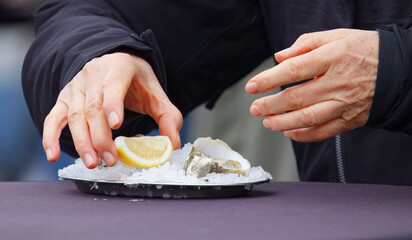 Hands arranging fresh oysters with lemon on crushed ice at the Naplavka farmers market in Prague.