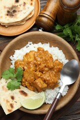 Delicious chicken tikka masala with rice, cilantro, lime and lavash served on wooden table, flat lay