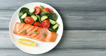 Piece of tasty grilled salmon, lemon, rosemary and salad on grey wooden table, top view. Space for text