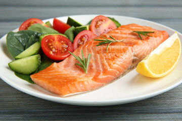 Piece of tasty grilled salmon, lemon, rosemary and salad on grey wooden table, closeup