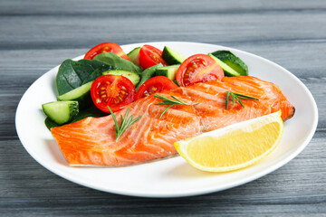 Piece of tasty grilled salmon, lemon, rosemary and salad on grey wooden table, closeup