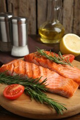 Pieces of tasty grilled salmon, rosemary and tomatoes on wooden table, closeup