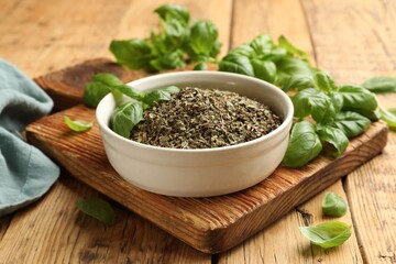 Dry basil in bowl and fresh green leaves on wooden table, closeup