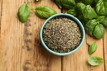 Dry basil in bowl and fresh green leaves on wooden table, flat lay. Space for text
