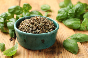Dry basil in bowl and fresh green leaves on wooden table, closeup