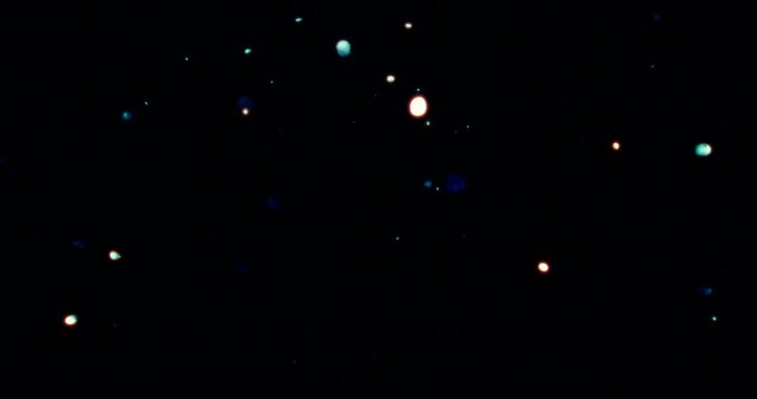 Particles float in water over a dark background, reflecting top light in green and blue hues, creating a glittering, halo-like, cosmic universe effect.
