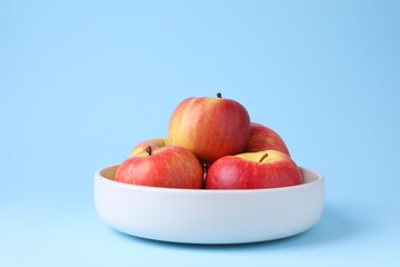 Ripe red apples in bowl on light blue background, closeup