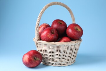 Ripe red apples and wicker basket on light blue background, closeup