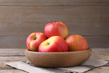 Ripe red apples in bowl on wooden table, closeup