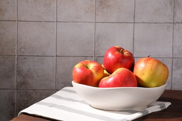 Ripe red apples in bowl on wooden table near grey tiled wall, closeup. Space for text