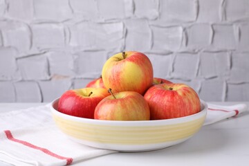 Ripe red apples in bowl on white table near grey textured wall, closeup