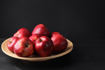 Ripe red apples on wooden table against black background, closeup. Space for text