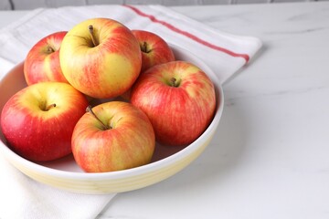 Ripe red apples in bowl on white table, closeup. Space for text