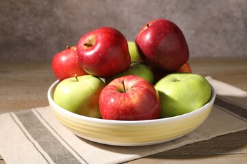 Fresh red and green apples in bowl on wooden table against grey background, closeup