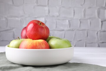 Fresh red and green apples in bowl on white wooden table near grey textured wall, closeup. Space for text