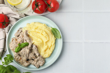 Delicious beef stroganoff with mashed potatoes and basil served on white tiled table, flat lay. Space for text