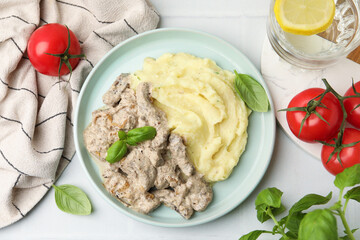 Delicious beef stroganoff with mashed potatoes and basil served on white tiled table, flat lay
