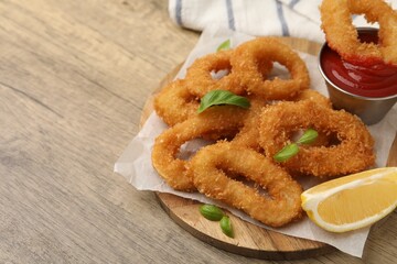 Deep fried squid rings with lemon slice, basil and ketchup on wooden table, closeup. Space for text