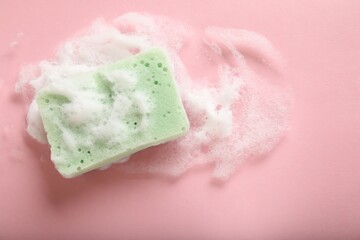 Kitchen sponge with foam on pink background, top view