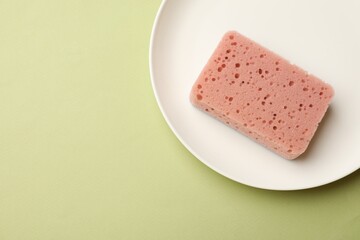 Kitchen sponge and plate on light green background, top view. Space for text