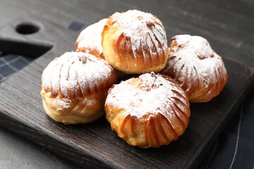 Tasty profiteroles with powdered sugar on black table, closeup