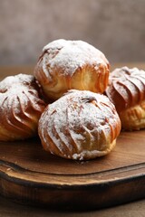 Tasty profiteroles with powdered sugar on wooden table, closeup