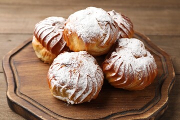 Tasty profiteroles with powdered sugar on wooden table, closeup