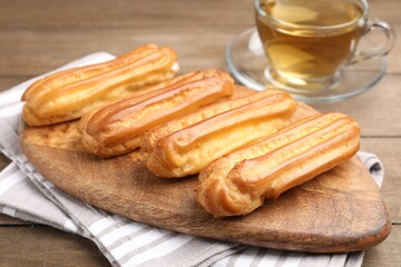 Tasty eclairs and tea on wooden table, closeup