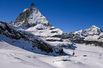 Iconic Matterhorn peak covered in winter snow, rising sharply against a clear deep blue sky. Dramatic alpine landscape with rugged cliffs and glacier textures.