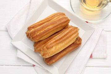 Tasty eclairs and tea on white wooden table, flat lay